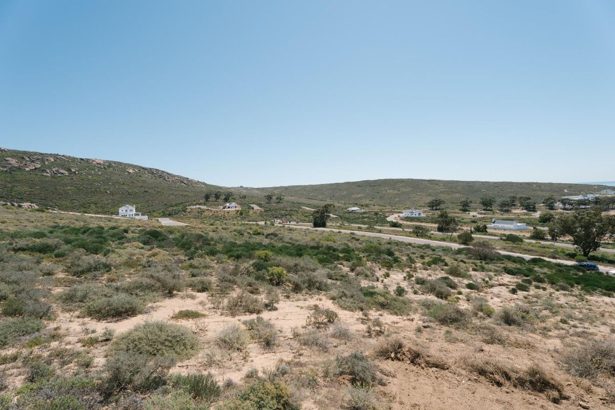 A wide-angle view of the vacant residential land, showcasing the natural topography, surrounding coastal vegetation, and distant neighborhood development.