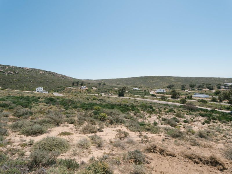 A wide-angle view of the vacant residential land, showcasing the natural topography, surrounding coastal vegetation, and distant neighborhood development.