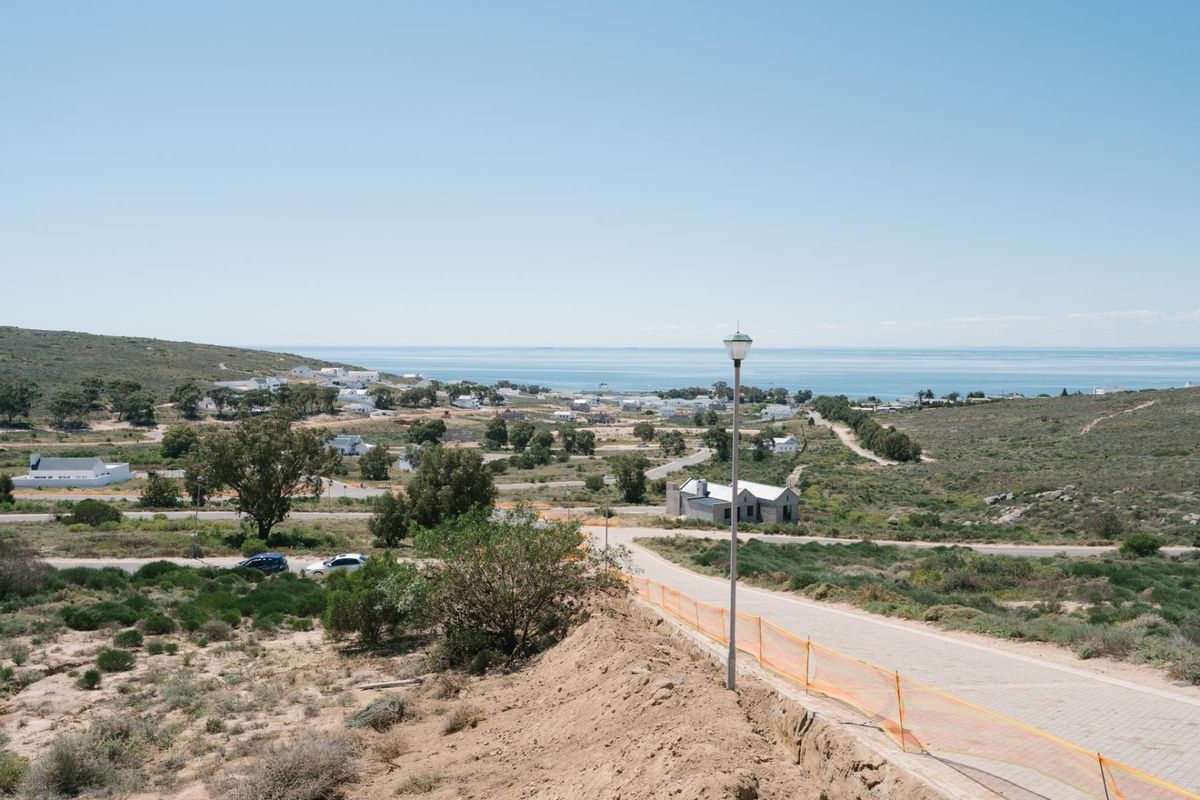 Elevated view overlooking a coastal residential area with paved roads, street lighting, and distant ocean vistas.