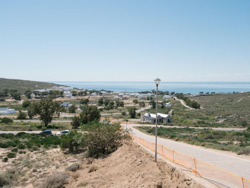 Elevated view overlooking a coastal residential area with paved roads, street lighting, and distant ocean vistas.