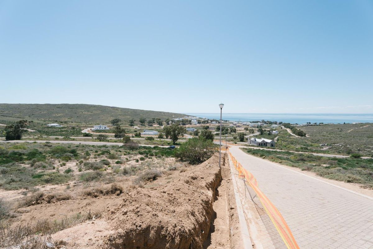 Elevated view overlooking a coastal residential area with a paved road, street lighting, and ongoing infrastructure work in the foreground.
