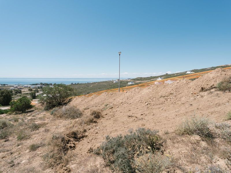 A view of the vacant residential land featuring sloping terrain, natural vegetation, and distant coastal scenery under a clear blue sky.