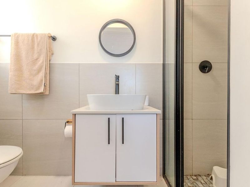 Modern bathroom featuring a vessel sink on a vanity cabinet, a glass-enclosed shower, and neutral wall tiling.
