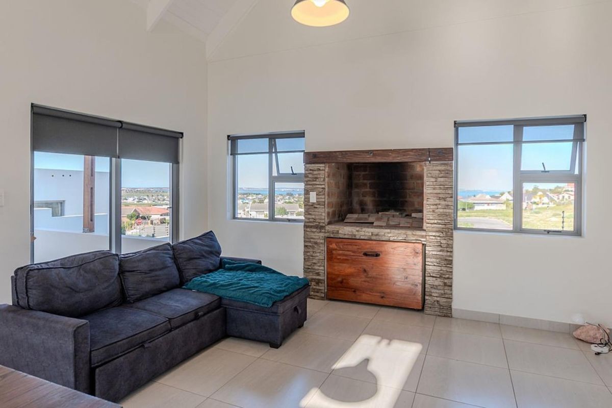Spacious living area featuring a built-in indoor braai with stone cladding, vaulted ceilings, tiled floors, and large windows offering scenic neighbourhood views.