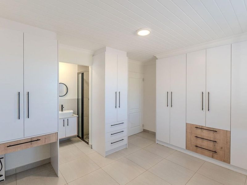 Spacious bedroom featuring extensive built-in cabinetry with modern finishes, tiled flooring, and direct access to an en-suite bathroom.