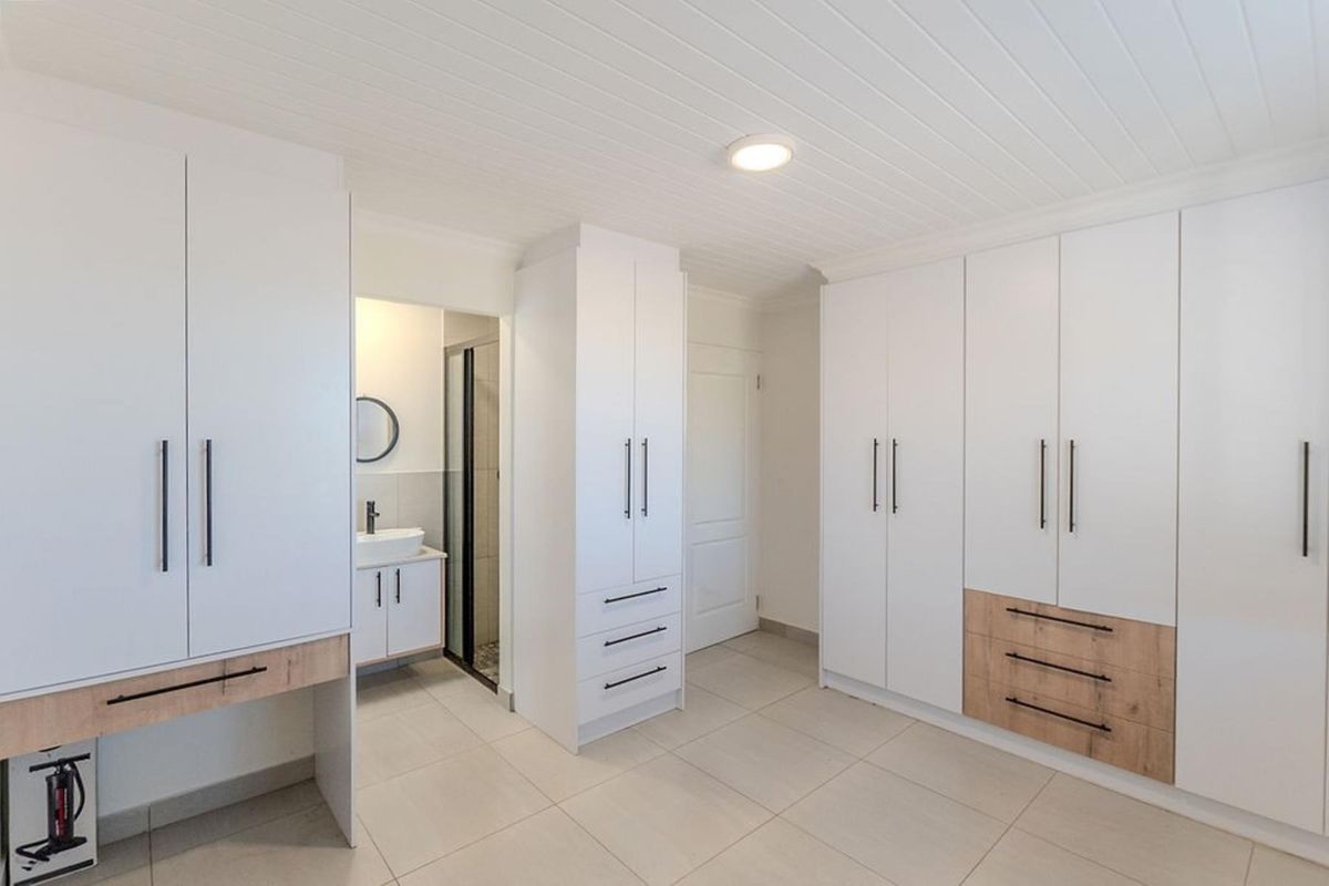 Spacious bedroom featuring extensive built-in cabinetry with modern finishes, tiled flooring, and direct access to an en-suite bathroom.