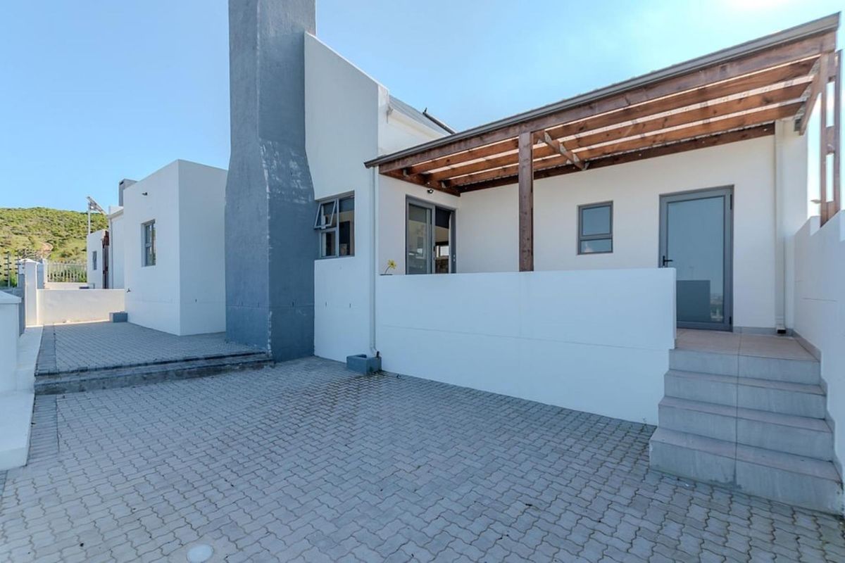 Rear exterior view of the townhouse featuring a paved courtyard, a timber pergola, and an external chimney stack.