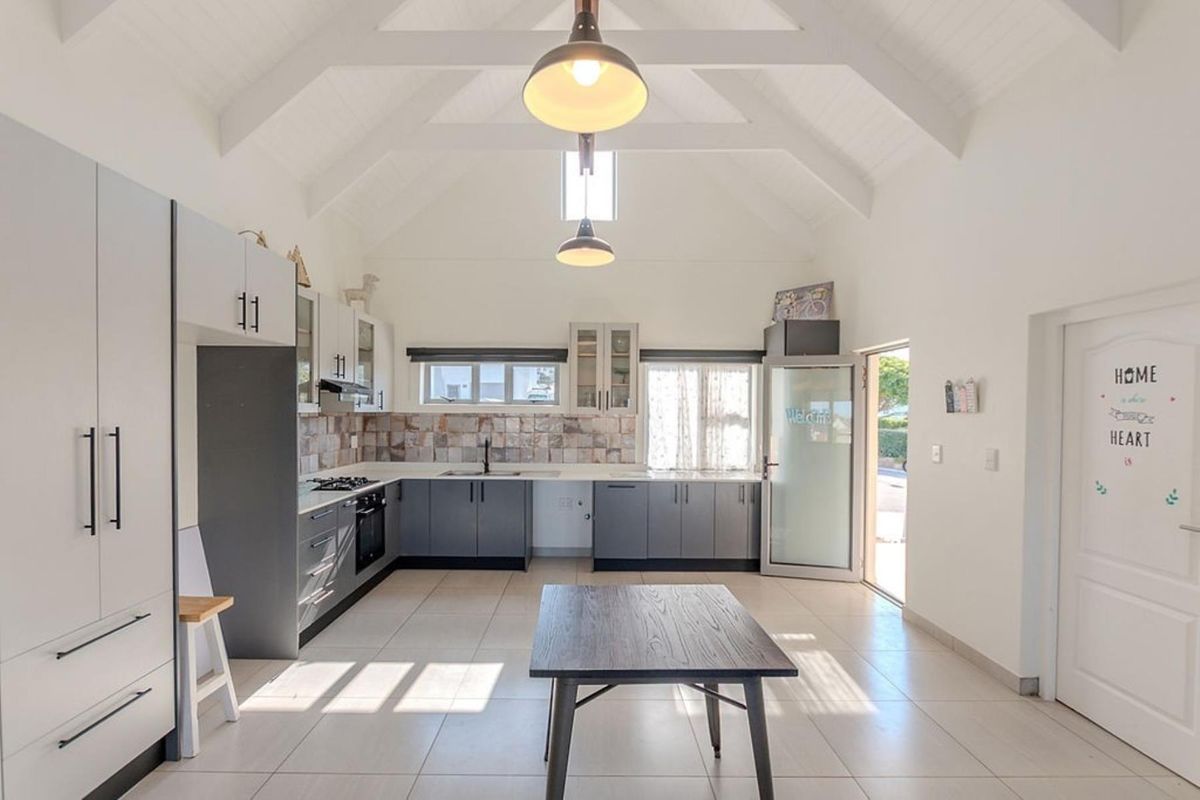 Modern kitchen featuring a high vaulted ceiling, sleek grey cabinetry, tiled backsplash, and integrated appliances, offering a bright and spacious culinary environment.