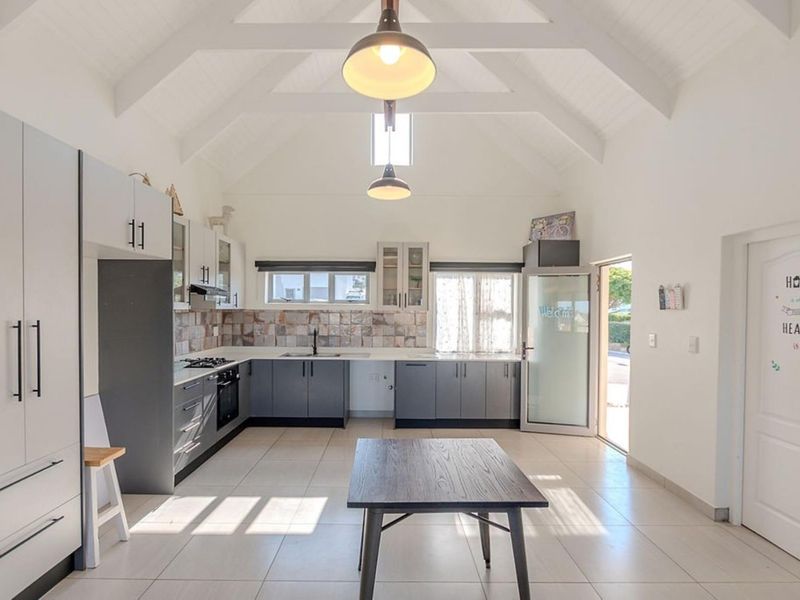 Modern kitchen featuring a high vaulted ceiling, sleek grey cabinetry, tiled backsplash, and integrated appliances, offering a bright and spacious culinary environment.