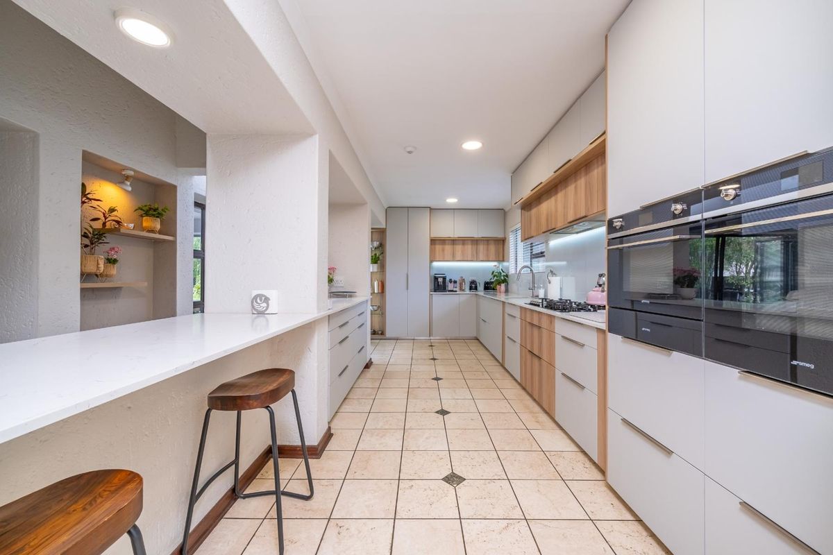 Modern kitchen featuring sleek cabinetry, stone countertops, integrated appliances including dual ovens, and a breakfast bar with recessed lighting.