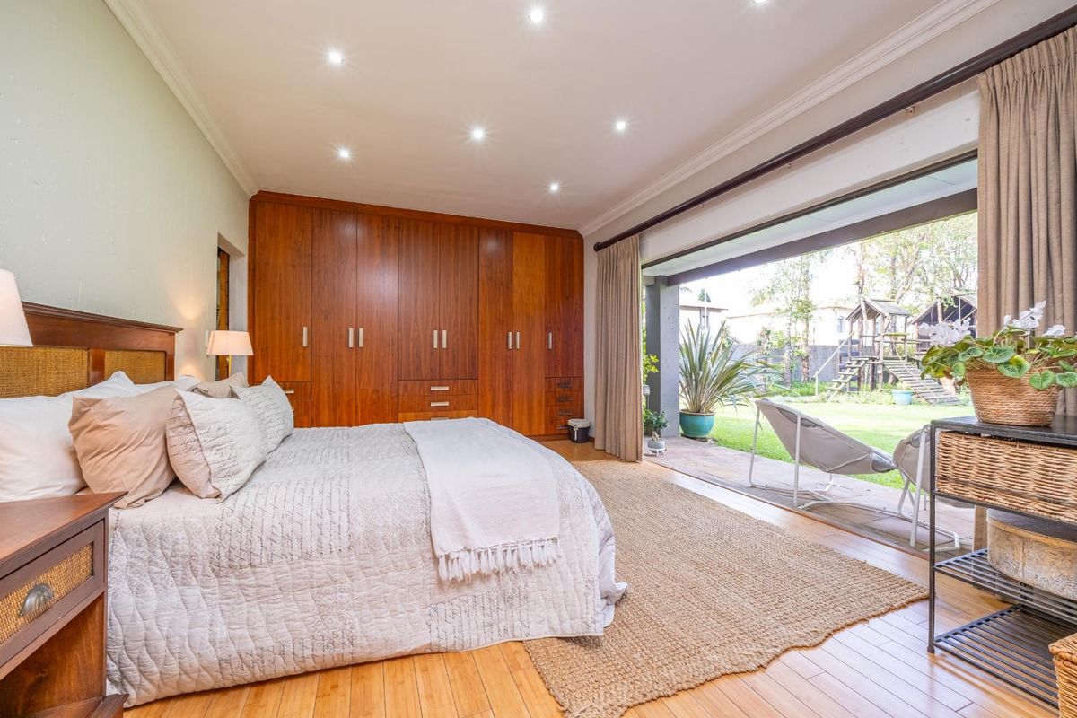 Spacious bedroom featuring extensive built-in wooden cabinetry, recessed lighting, and large sliding doors opening onto a private patio and garden.