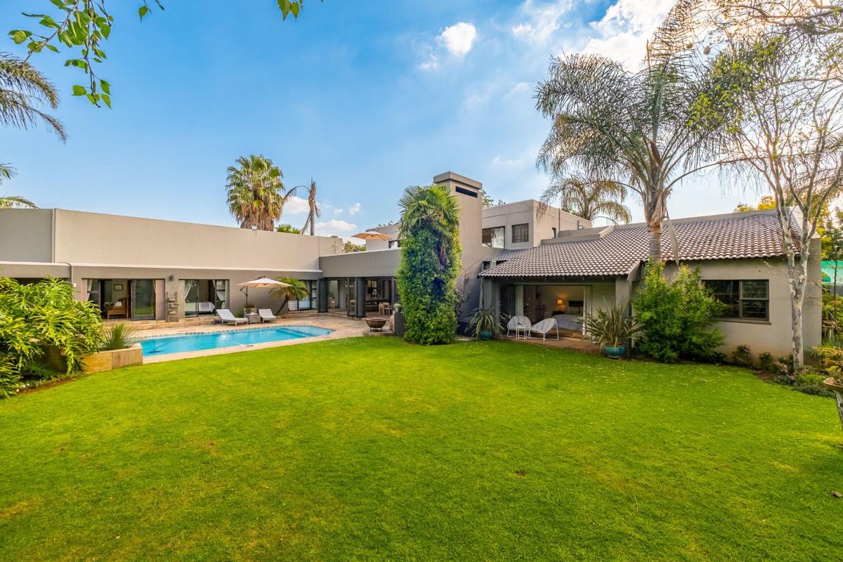 Spacious rear garden featuring a well-maintained swimming pool, lush lawn, and direct access to the home through multiple sliding glass doors.