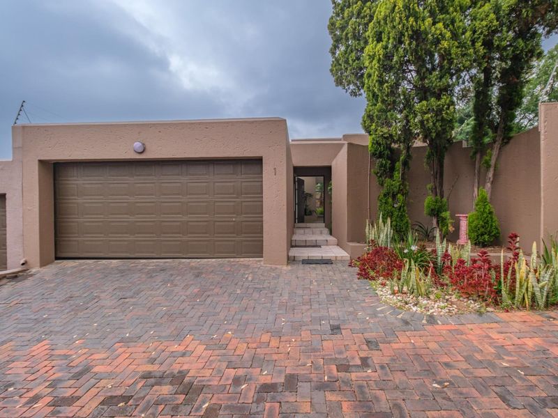 Front elevation of the property featuring a paved driveway, double garage, and established garden beds.