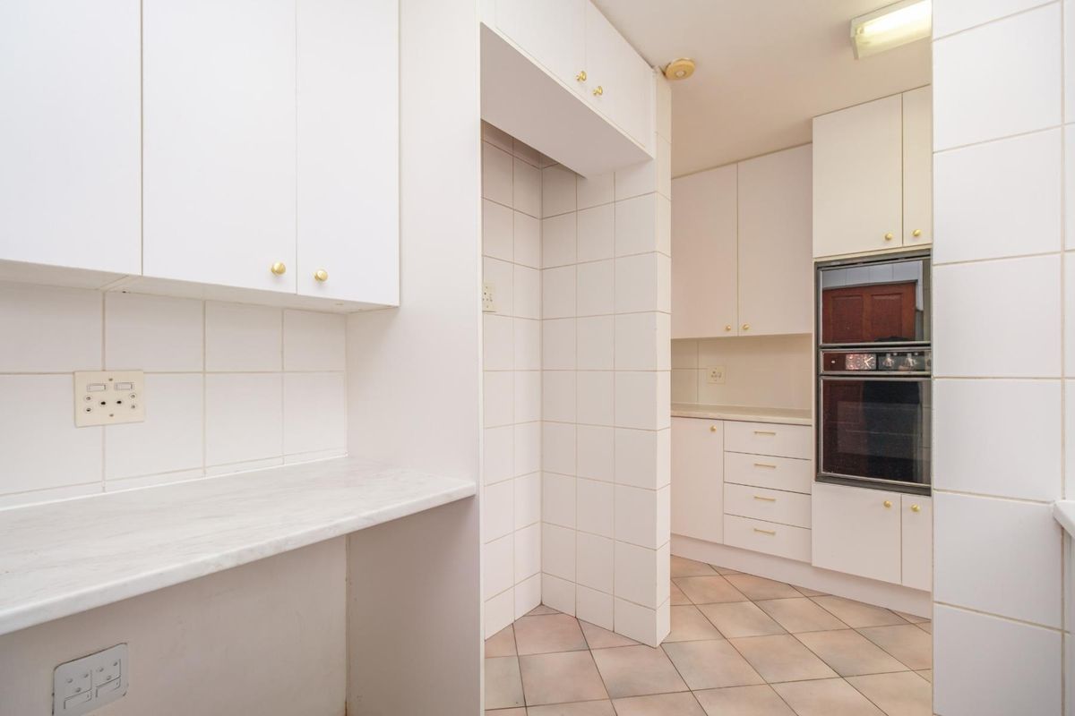 A functional, empty kitchen featuring white built-in cabinetry, tiled splashbacks, and a built-in oven, offering a clean canvas for potential updates.