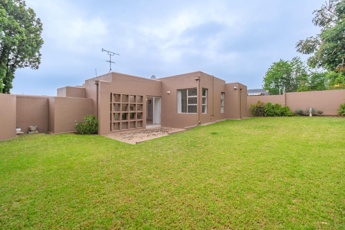 Rear view of the property featuring a private garden, a small paved patio area, and a decorative concrete screen wall.