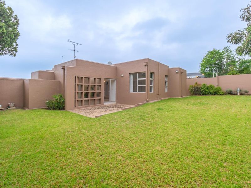 Rear view of the property featuring a private garden, a small paved patio area, and a decorative concrete screen wall.