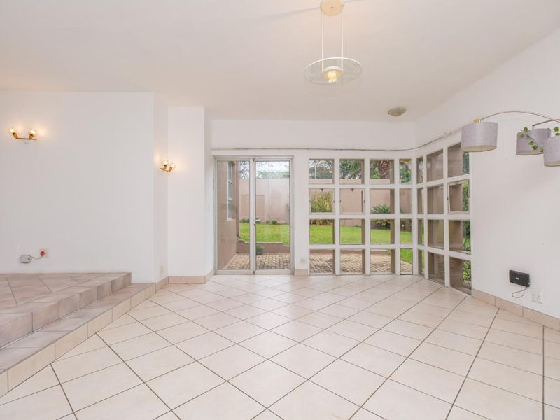 Spacious living area featuring large grid-pattern windows, tiled flooring, and a sliding glass door providing direct access to the rear garden.