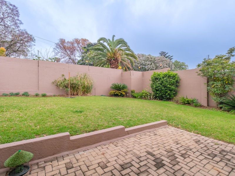 A well-maintained private garden featuring a paved patio area, lush lawn, and high perimeter boundary walls for added privacy.
