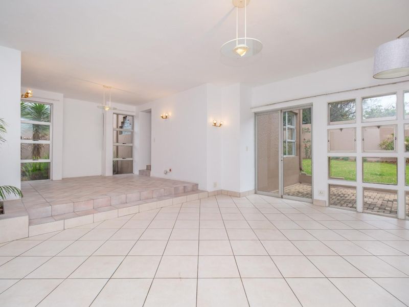Spacious, light-filled living area featuring a raised platform, tiled flooring, and large grid-pattern windows with direct access to the garden.