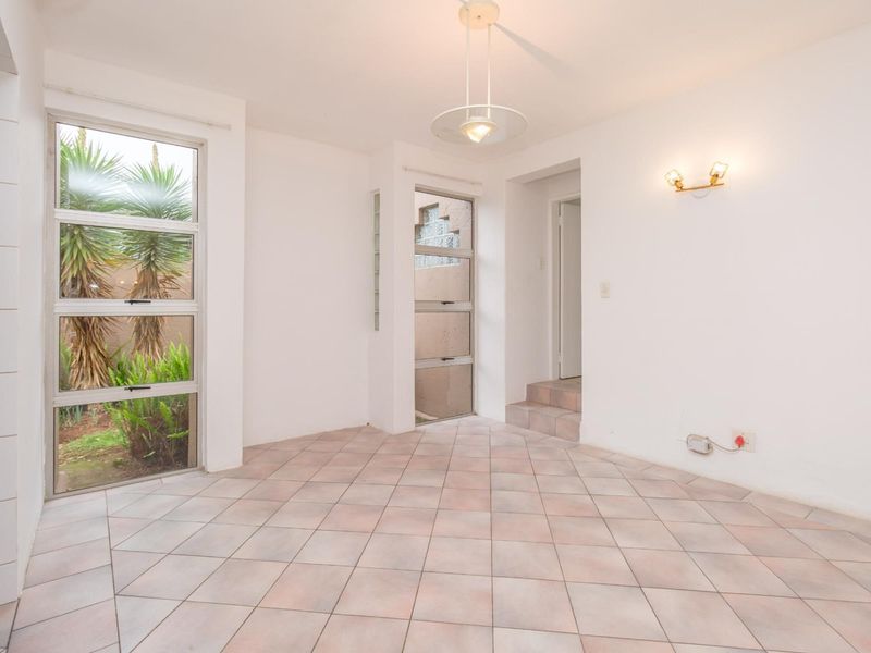 An empty, bright living area featuring tiled flooring, large aluminium windows with garden views, and integrated wall and ceiling lighting.