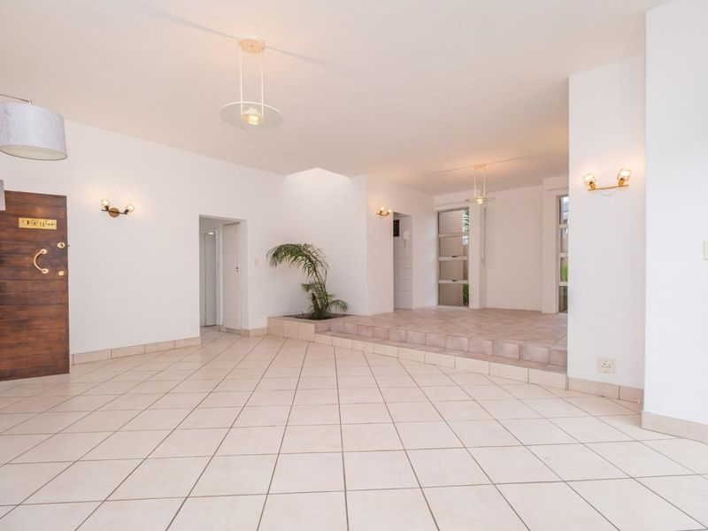 Spacious, light-filled living area featuring neutral tiled flooring, a raised platform section, and integrated lighting, offering a versatile open-plan layout.