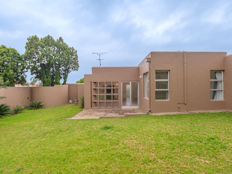 Rear view of the property featuring a paved patio area, established lawn, and boundary wall, with access via a sliding door.