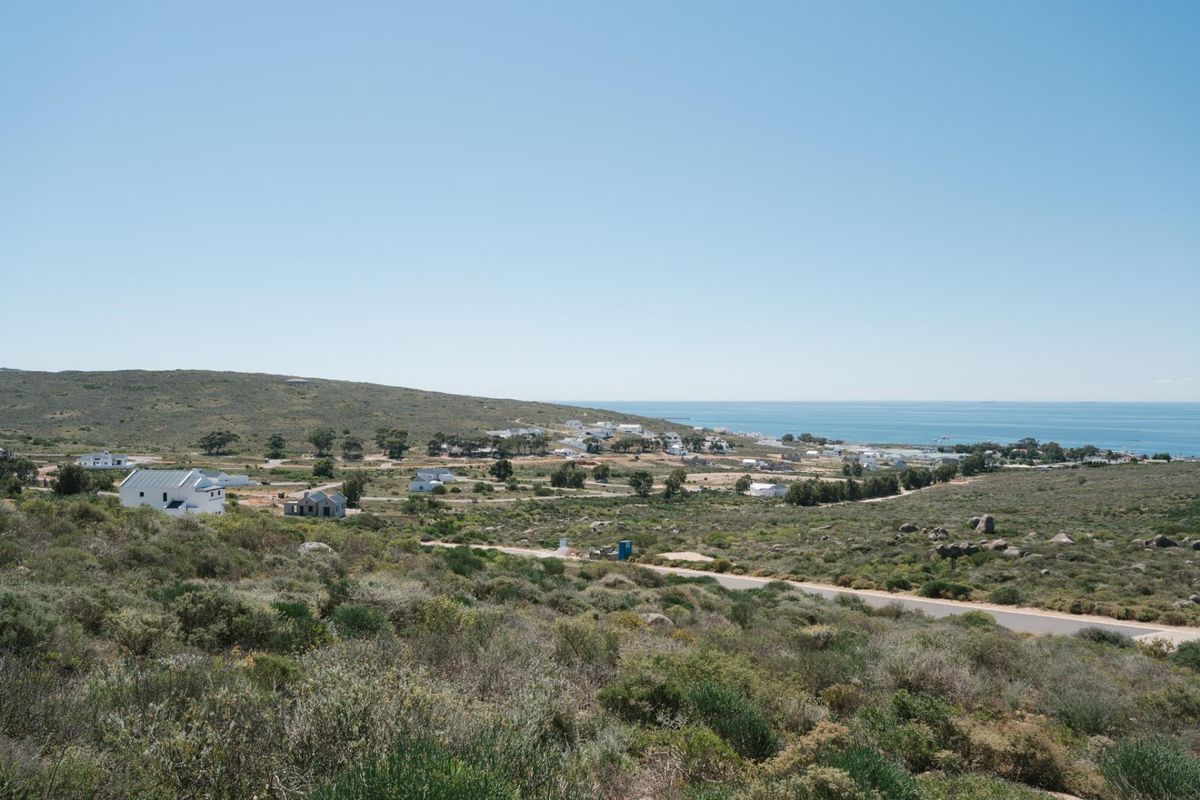 A scenic elevated view of the coastal landscape, featuring natural vegetation, scattered residential properties, and a clear view of the ocean.