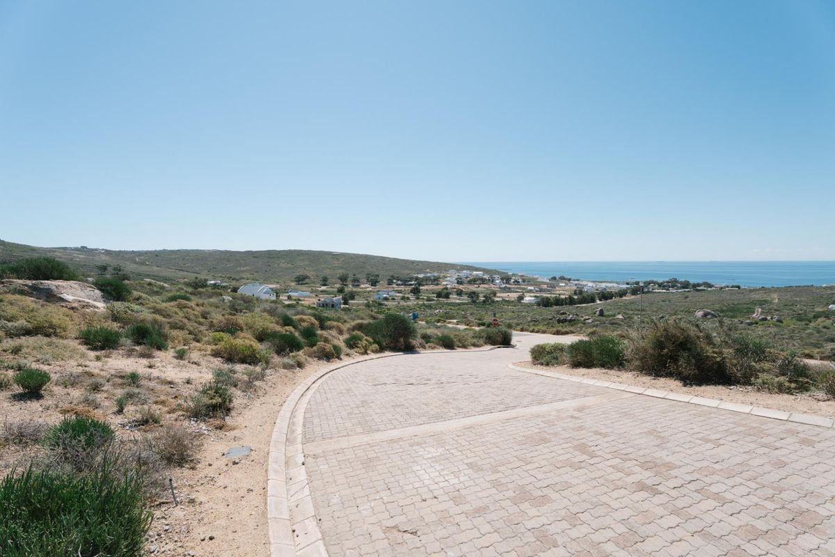 A view of a paved residential street leading towards a coastal landscape and the ocean in the distance.