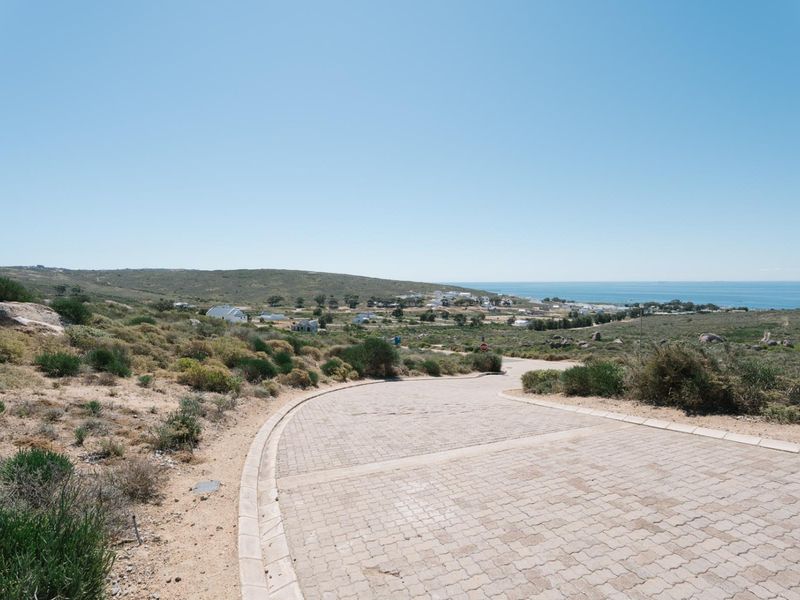 A view of a paved residential street leading towards a coastal landscape and the ocean in the distance.