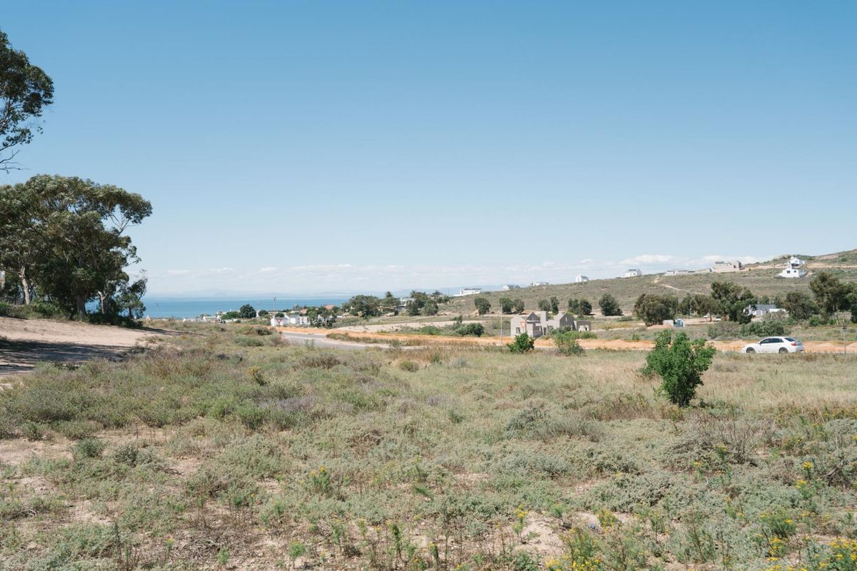 A scenic view overlooking a coastal landscape with natural vegetation, distant houses, and a glimpse of the ocean under a clear blue sky.