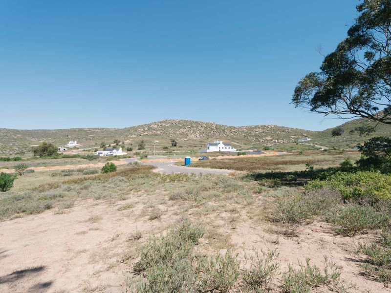 A wide-angle view of the vacant residential land, showcasing the surrounding natural landscape, hilly terrain, and nearby established residential properties.