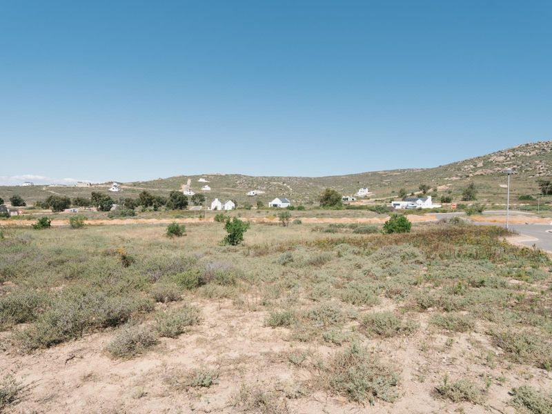 A wide-angle view of a vacant residential plot featuring natural coastal vegetation and surrounding hillside landscape with nearby road access.