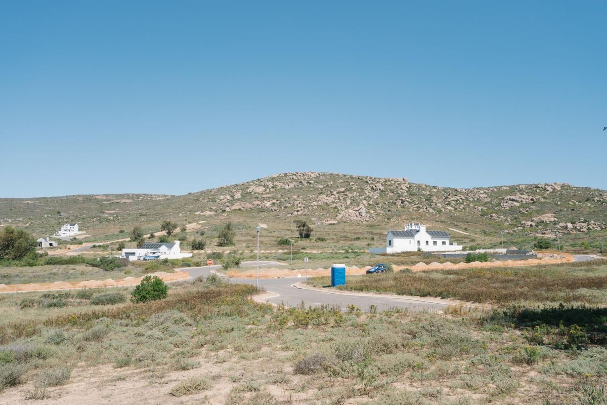An elevated view of a residential development site featuring paved roads and surrounding natural landscape with distant coastal homes.