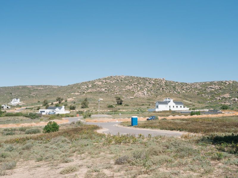 An elevated view of a residential development site featuring paved roads and surrounding natural landscape with distant coastal homes.