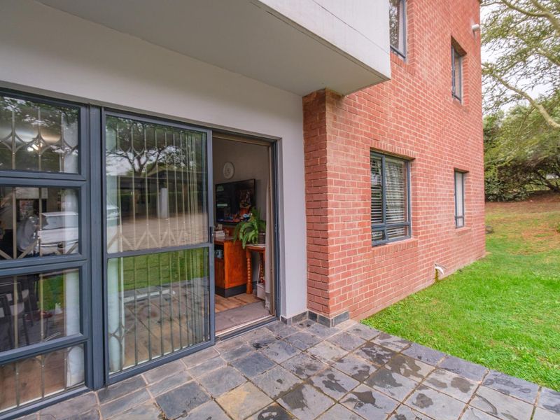 A covered patio area featuring slate tile flooring and a sliding glass door with security gate, providing direct access to the garden.