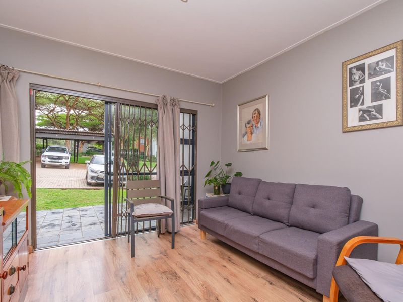 A comfortable living room featuring laminate flooring and a sliding glass door with a security gate, providing direct access to the exterior driveway area.