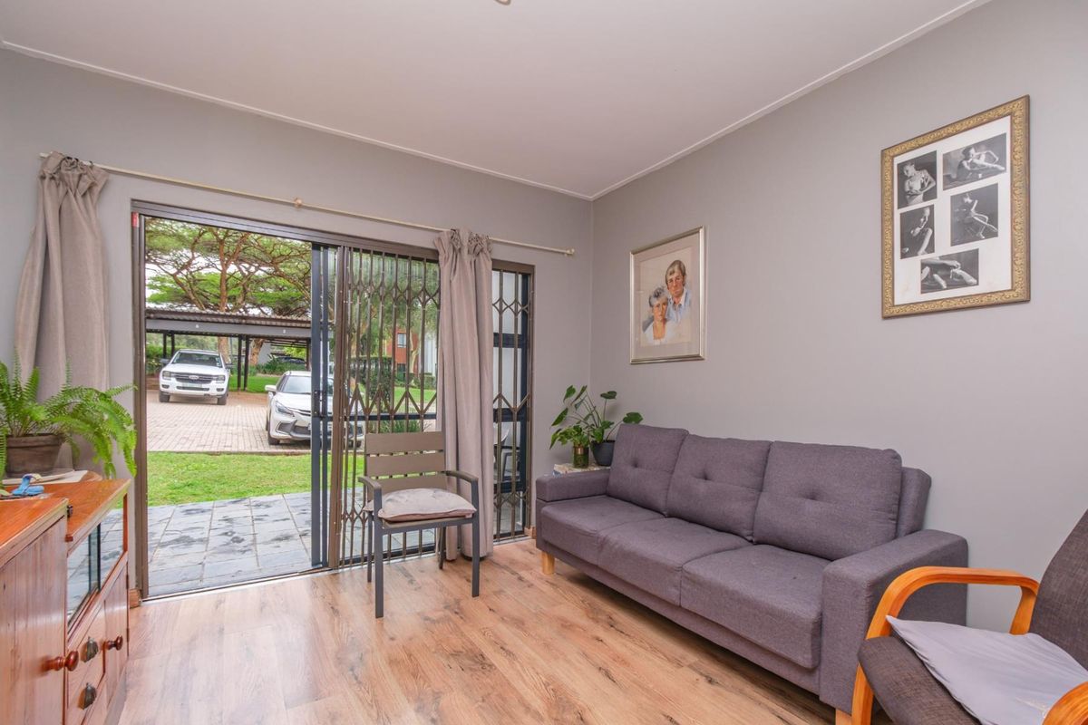 A comfortable living room featuring laminate flooring and a sliding glass door with a security gate, providing direct access to the exterior driveway area.