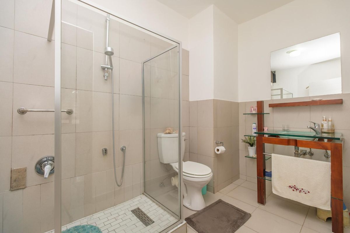 A functional bathroom featuring a glass-enclosed shower, a standard toilet, and a vanity basin with a wall-mounted mirror and tiled finishes.