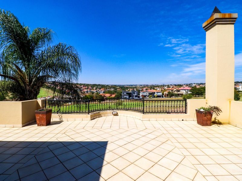 Spacious elevated balcony featuring tiled flooring, a decorative wrought iron balustrade, and a built-in chimney, offering expansive views of the surrounding estate.