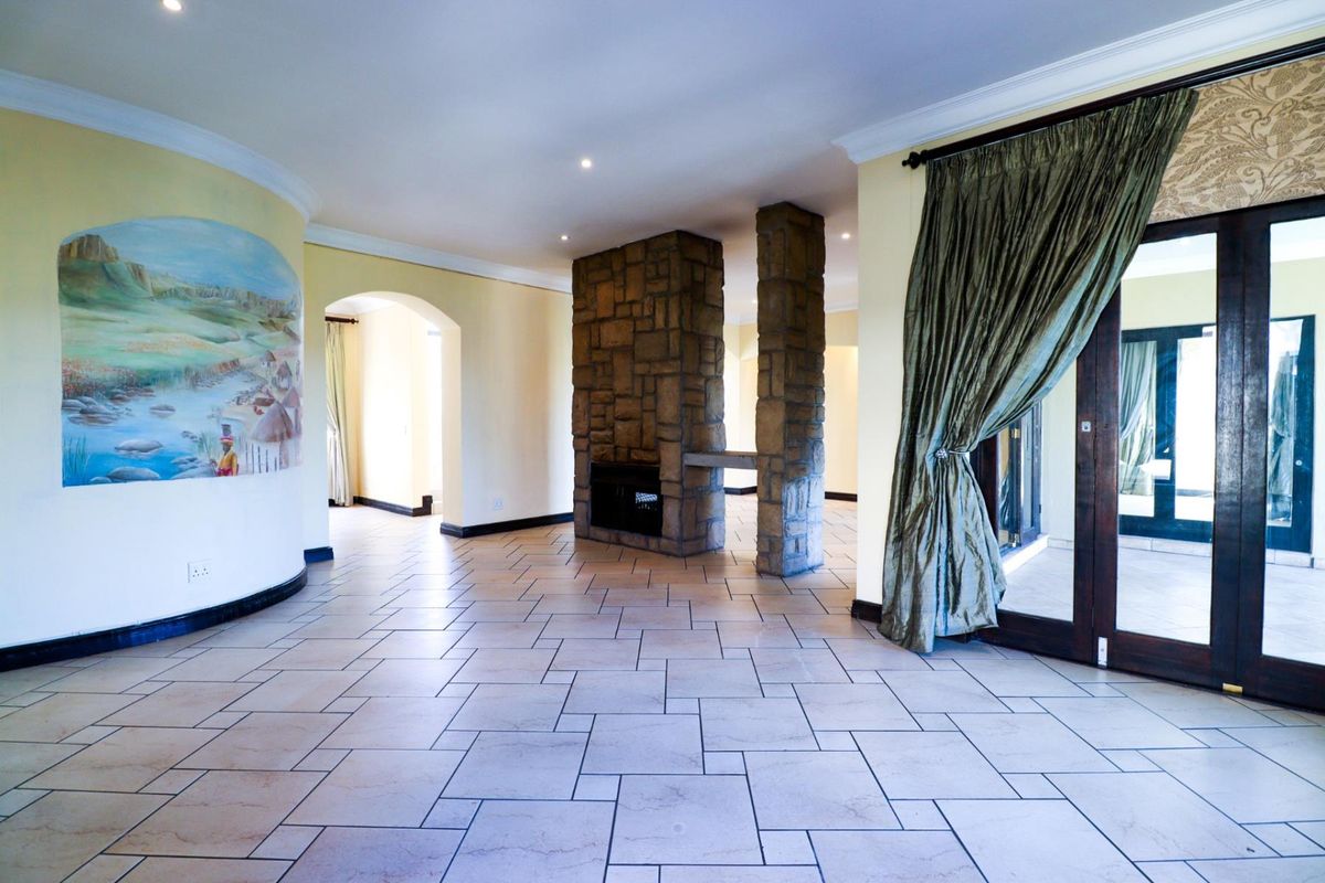 Spacious living area featuring a central stone-clad fireplace, tiled flooring, and double glass doors leading to an outdoor space.