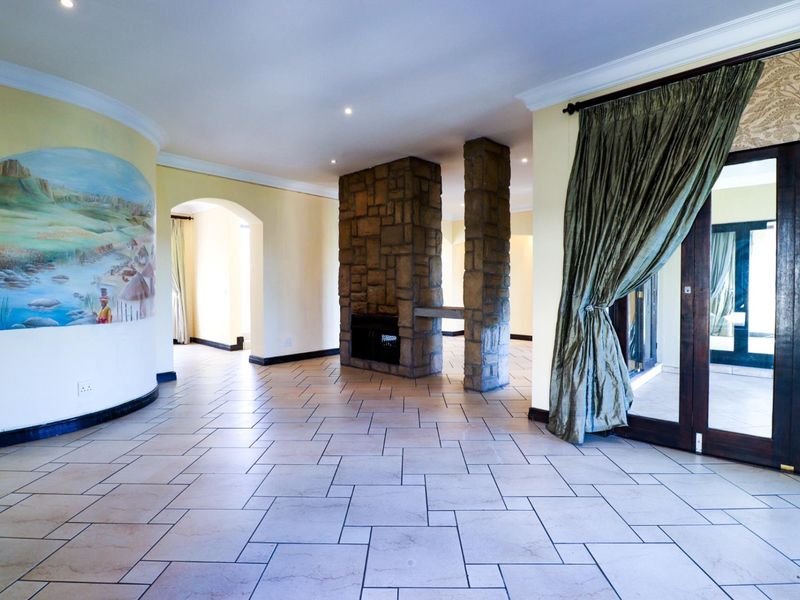Spacious living area featuring a central stone-clad fireplace, tiled flooring, and double glass doors leading to an outdoor space.