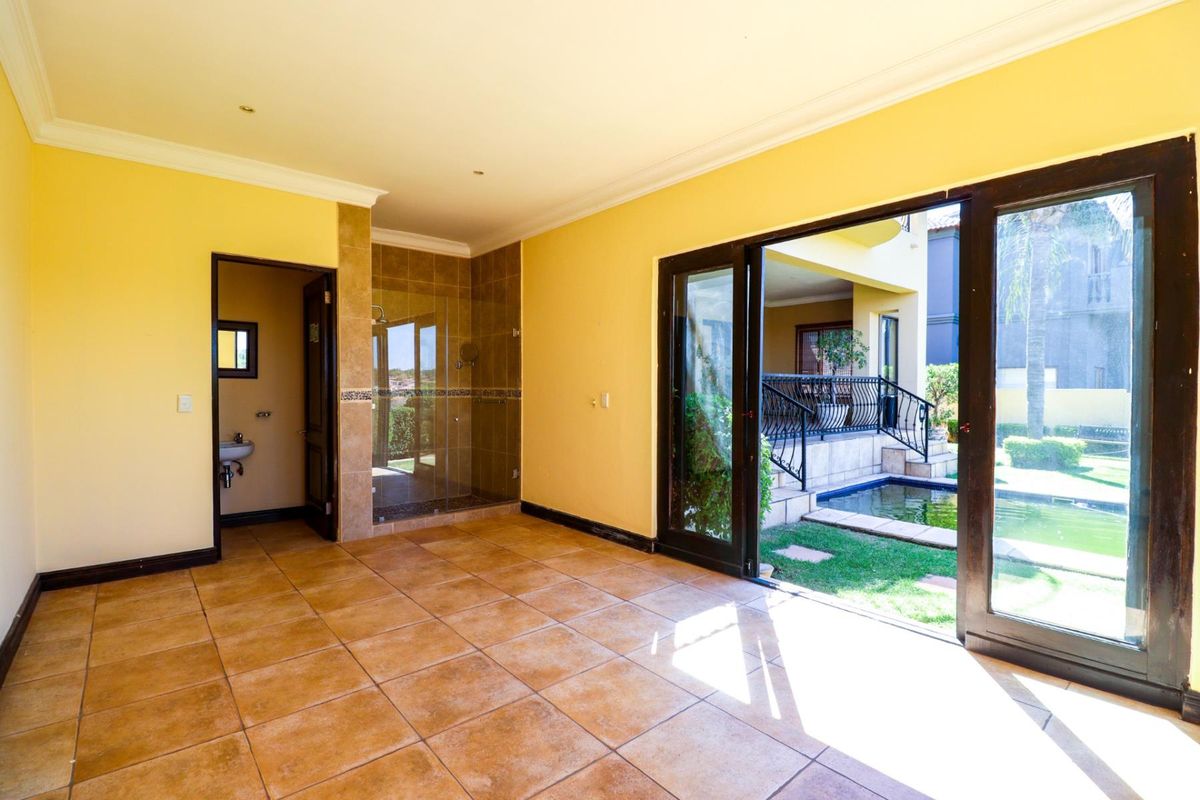 Spacious bedroom featuring tiled flooring, an en-suite bathroom with a glass shower, and large sliding doors opening to a private patio and pool area.