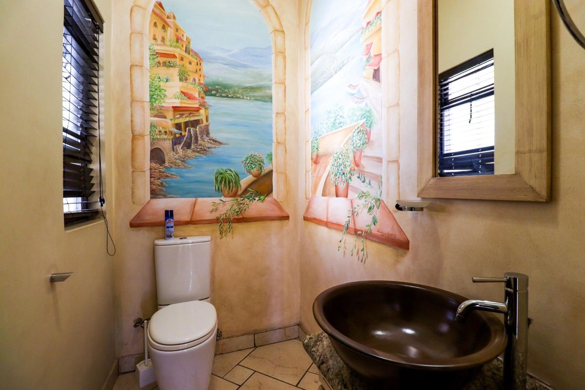 A compact guest bathroom featuring a vessel sink on a stone vanity, a modern toilet, and decorative wall murals.