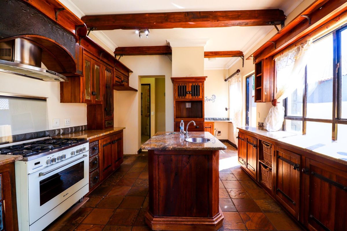 A rustic-style kitchen featuring extensive wooden cabinetry, granite countertops, a central island, and exposed ceiling beams, providing a warm and traditional aesthetic.