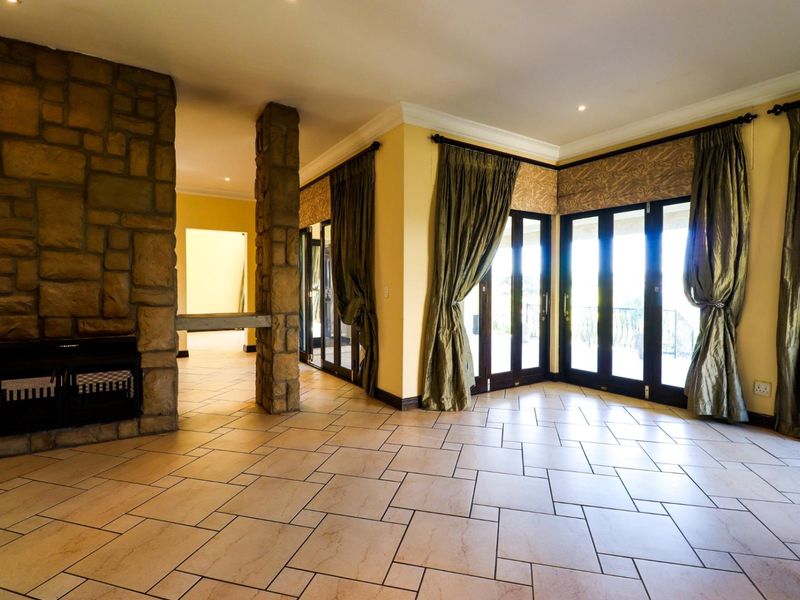 Spacious living area featuring a prominent stone fireplace, stone pillar, tiled flooring, and multiple sets of french doors leading to the exterior.