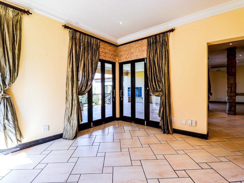 Spacious living area featuring neutral tiled flooring, coved cornicing, and double glass doors providing access to an outdoor patio area.