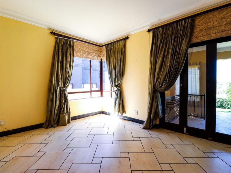 A bright, empty living area featuring tiled flooring, corner windows, and a sliding glass door providing access to an outdoor space.
