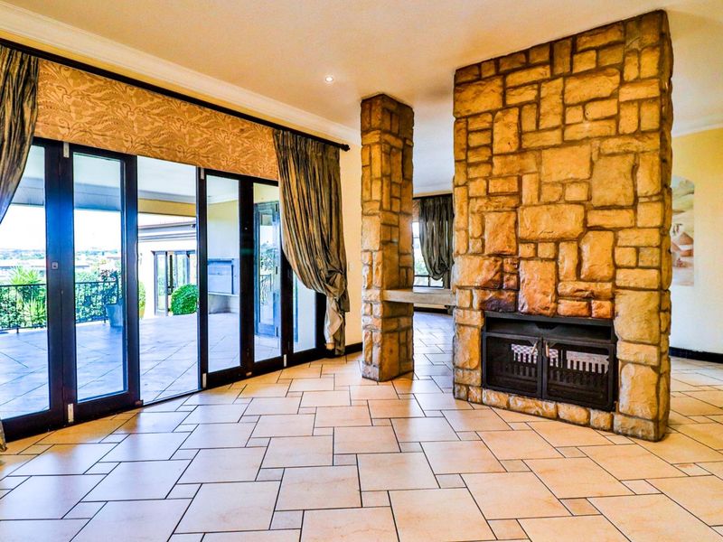 Spacious living area featuring a prominent stone fireplace, stone pillar, tiled flooring, and large sliding glass doors opening to an outdoor patio.