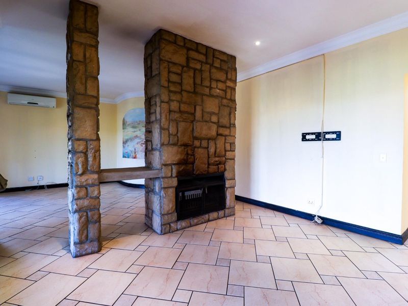 Spacious living area featuring a prominent stone-clad fireplace and pillar, ceramic tile flooring, and a wall-mounted air conditioning unit.