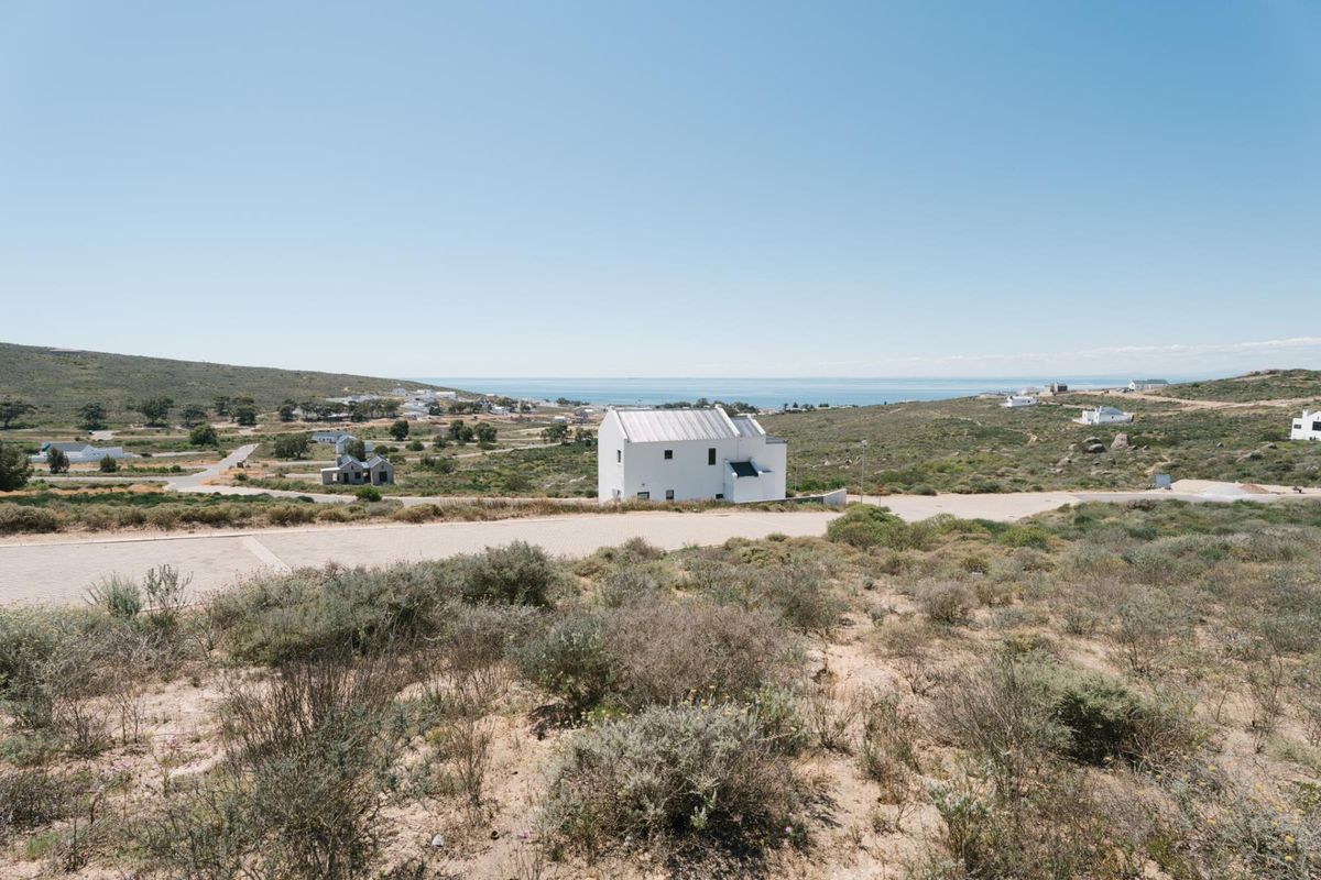 An elevated aerial view of a vacant residential plot featuring natural coastal vegetation, gravel access roads, and distant ocean views.
